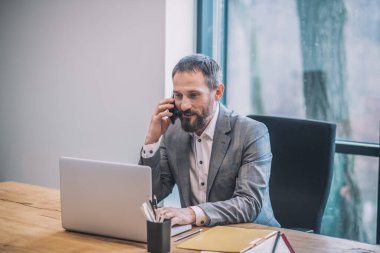 Akıllı telefonda dizüstü bilgisayarın önünde konuşan adam.