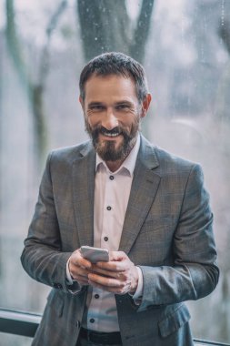 Akıllı telefonlu, iş elbiseli neşeli bir adam.