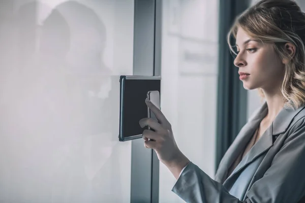 Woman touching smartphone to intercom at office — Stock Photo, Image