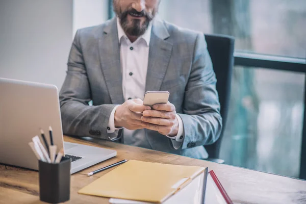 Zakenman met smartphone in handen zittend op kantoor — Stockfoto