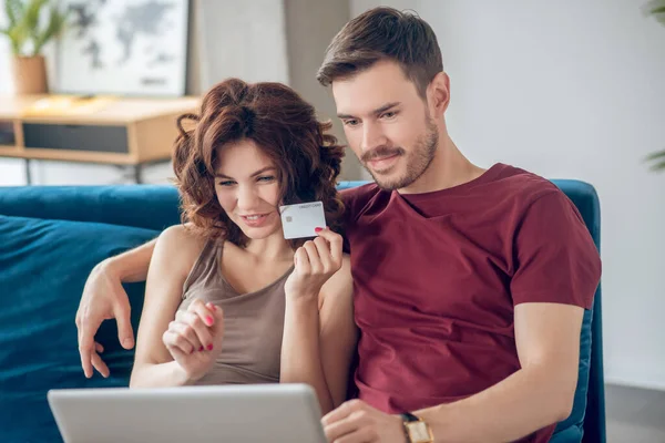 若いカップルはソファに座ってオンラインで製品を選択します — ストック写真