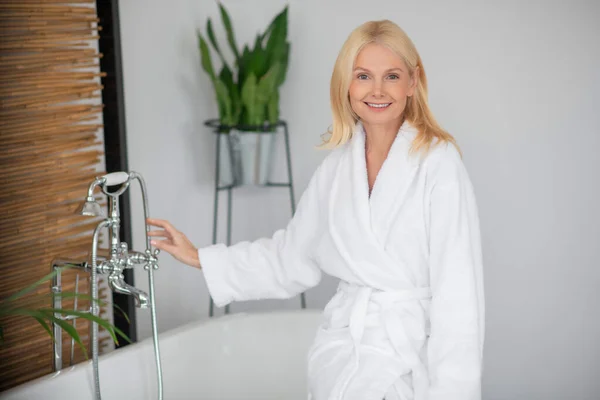 Blonde hübsche Frau im weißen Bademantel im Badezimmer — Stockfoto