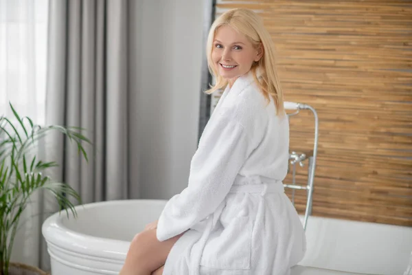 Blonde hübsche Frau in weißem Bademantel bereitet die Badewanne vor — Stockfoto