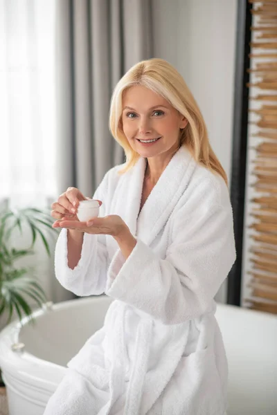 Eine Frau im weißen Bademantel mit einem Glas Gesichtscreme — Stockfoto