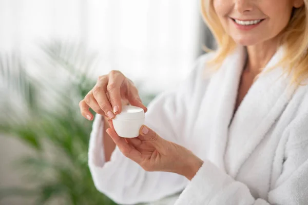 Una mujer con una bata blanca sosteniendo un frasco de crema facial — Foto de Stock