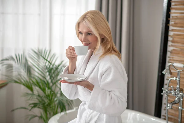Goed uitziende blonde vrouw die thee drinkt en er evenwichtig uitziet — Stockfoto