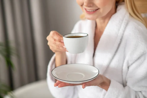 하얀 가운을 입고 아침 커피를 마시며 뿌듯 해 보이는 여자 — 스톡 사진