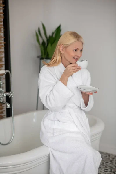 Donna in vestaglia bianca avendo il suo caffè del mattino e guardando soddisfatto — Foto Stock
