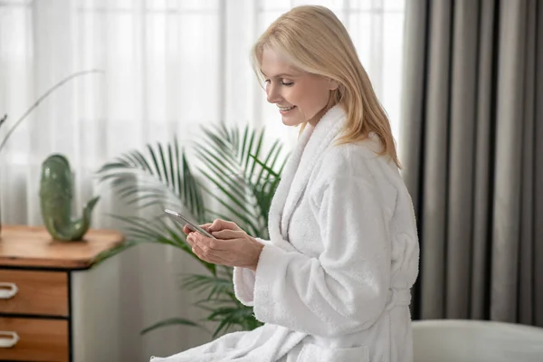 Жінка в білому халаті смс на смартфоні — стокове фото