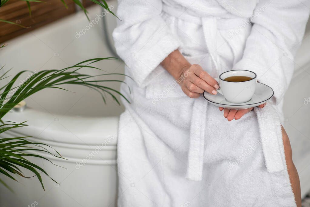 Woman in a white robe holding a cup with tea