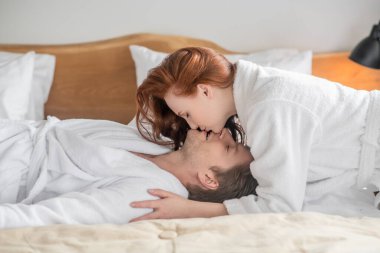 Beyaz bornozlu bir çift yatakta yatıyor ve birbirlerine aşık oluyorlar.