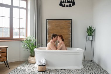 Bir adam ve bir kadın birlikte banyo yapıyor, öpüşüyor ve sarılıyorlar.