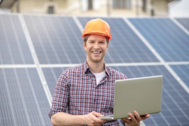 Dizüstü bilgisayarlı, koruyucu kasklı mutlu bir adam.