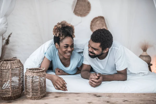 Темнокожий улыбающийся мужчина и женщина лежат под одеялом — стоковое фото