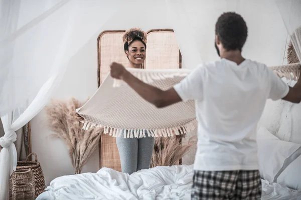 Dunkelhäutige Frau und Mann stehen mit Decke in Bettnähe — Stockfoto