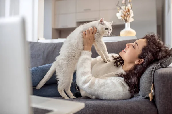 Молода жінка лежить на дивані зі своєю кішкою і виглядає розслабленою — стокове фото