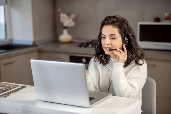 Egy fülhallgatós operátor ül a laptopnál, miközben otthonról dolgozik. — Stock Fotó