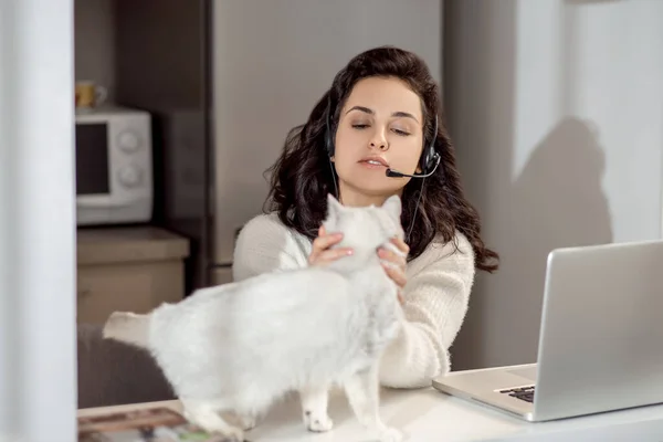 Uma mulher em fones de ouvido sentada no laptop enquanto trabalhava em casa — Fotografia de Stock