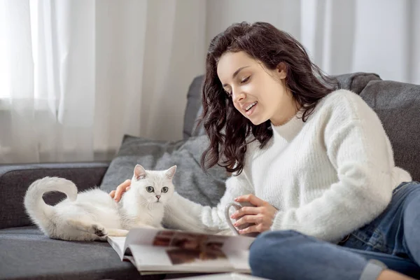 Молодая женщина отдыхает дома со своей кошкой и выглядит расслабленной — стоковое фото