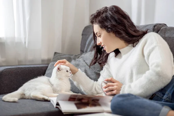Eine Frau ruht sich zu Hause aus, liest Zeitschriften und streichelt ihre Katze — Stockfoto