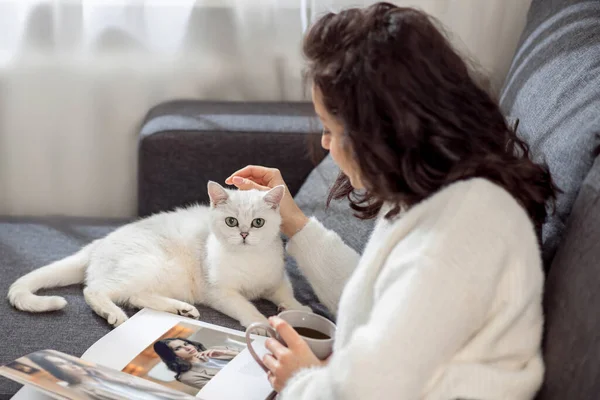 Eine Frau ruht sich zu Hause aus, liest Zeitschriften und streichelt ihre Katze — Stockfoto