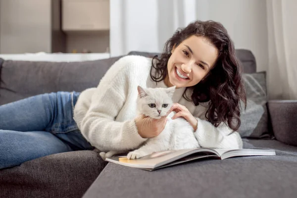 Söt kvinna som ligger på soffan och smeker sin söta vita katt — Stockfoto