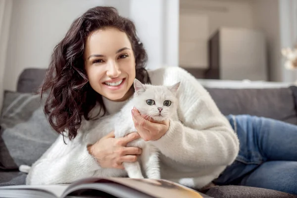 Femme mignonne allongée sur le canapé et caressant son chat blanc mignon — Photo