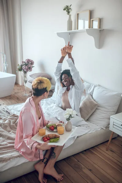 Mulher com bandeja de pequeno-almoço e acordar namorada — Fotografia de Stock