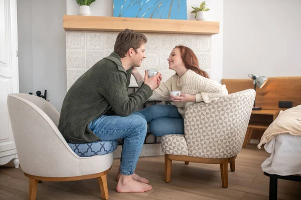 Smiling man and touching woman drinking coffee near fireplace — Stock Photo, Image