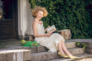 Genç bir kadın elinde kitapla merdivenlerde oturuyor.