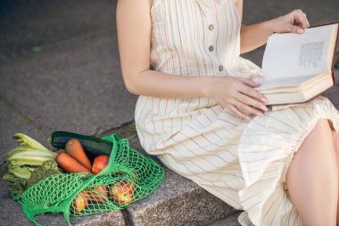 Merdivenlerde elinde kitapla oturan bir kadın.