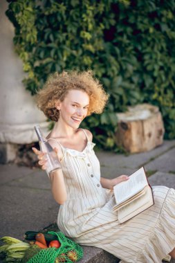 Genç bir kadın elinde bir şişe suyla merdivenlerde oturuyor.