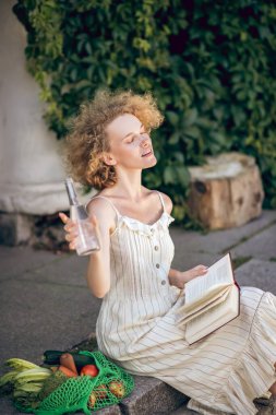 Genç bir kadın elinde bir şişe suyla merdivenlerde oturuyor.