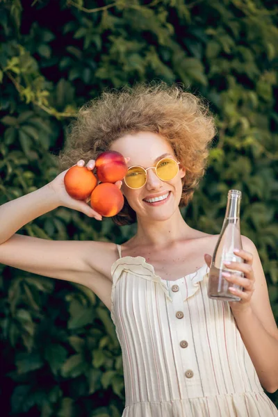 Mujer joven rizada con nectarinas que parecen felices —  Fotos de Stock