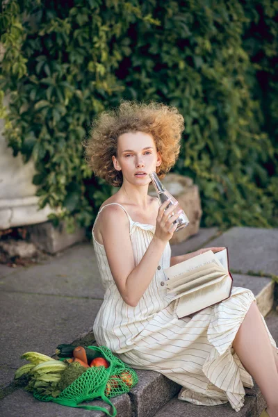 Jonge vrouw zittend op de trap met een fles water in handen — Stockfoto