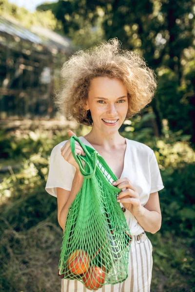 Jong meisje met een groene mesh zak met fruit in handen — Stockfoto