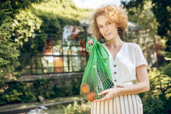 Giovane ragazza con una borsa a rete verde con frutta in mano — Foto Stock