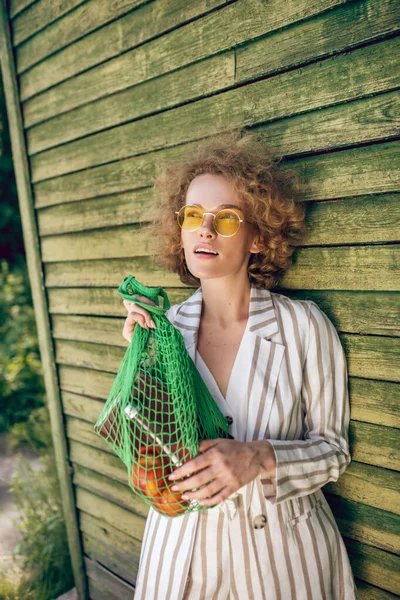 Bild på en ung kvinna i solglasögon med nätväska — Stockfoto