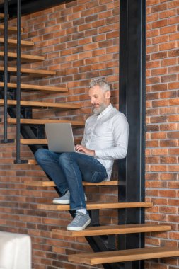 Gray-haired man sitting on the stairs with a laptop
