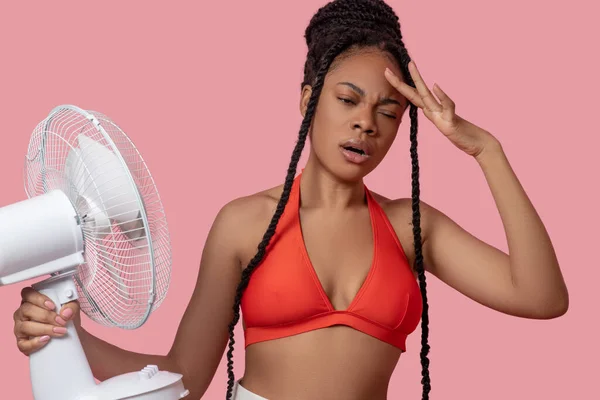 Lächelnde Afroamerikanerin hält einen Ventilator in der Hand, der von Hitze müde aussieht — Stockfoto