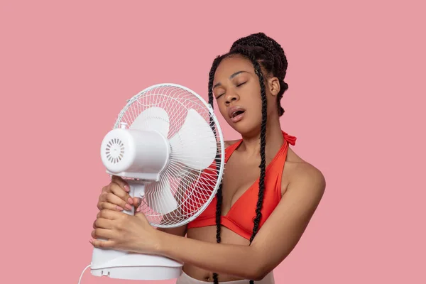 Sorrindo afro-americana segurando um ventilador olhando cansado do calor — Fotografia de Stock