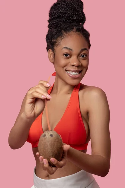 Mulher de pele escura segurando coco e parecendo feliz — Fotografia de Stock