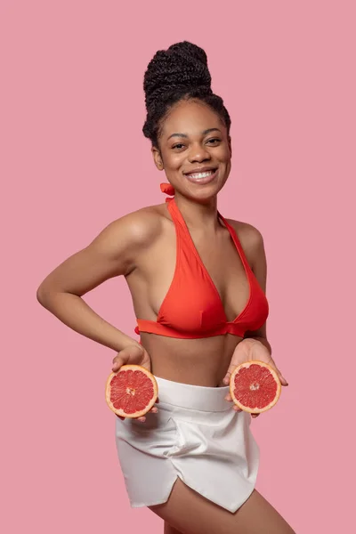 Dark-skinned woman holding grapefruit slices and looking happy — Stock Photo, Image