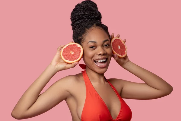 Mörkhyad kvinna som håller i grapefruktskivor och ser glad ut — Stockfoto
