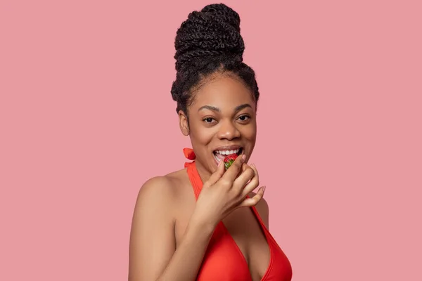 Dark-skinned woman eating strawberries and looking enjoyed — Stock Photo, Image