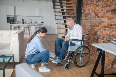 Dark-haired young woman helping her handicapped husband to tie his snickers