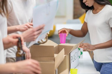 Esmer tenli kız kullanılmış plastiği kutuya ayırıyor.