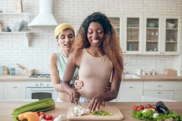 Donkere vrouw hakken groenten en vriendin van achteren — Stockfoto