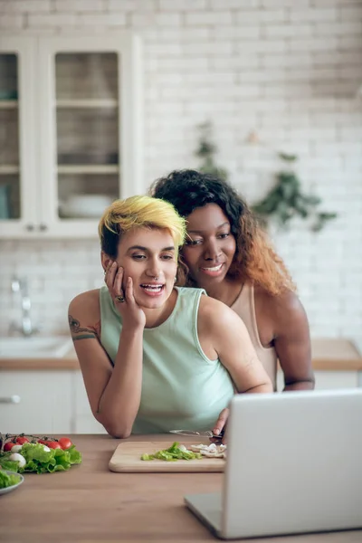 Caucasian woman and dark skinned girlfriend smiling near laptop — ストック写真