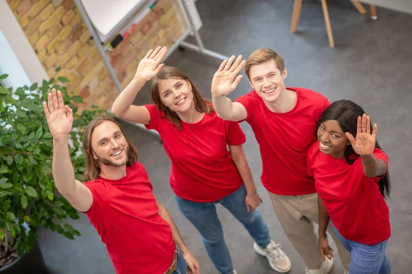Squadra di giovani volontari che salutano mano mentre in piedi in casa — Foto Stock